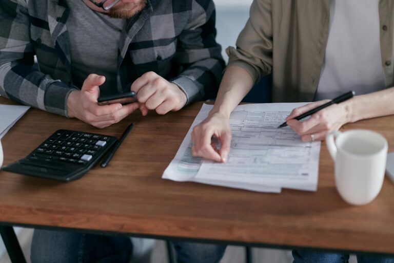 A couple diligently reviews their finances using a calculator and documents at home.