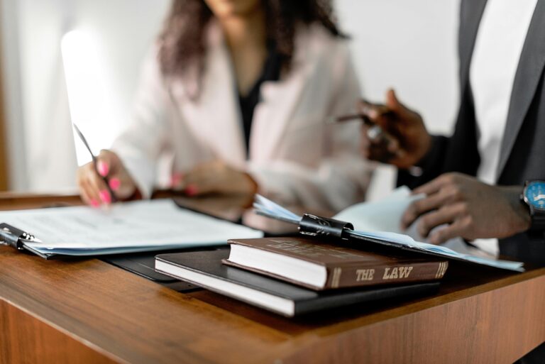 Two lawyers reviewing documents with law books on a desk. Professional legal environment.