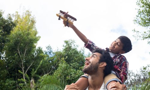 Boy playing with airplane while sitting on fathers shoulder